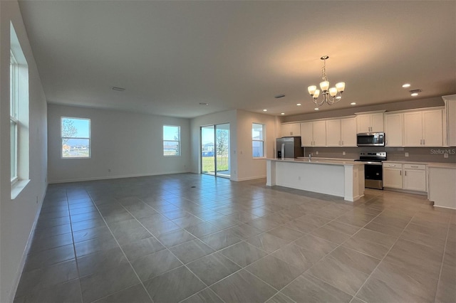 kitchen with light tile patterned flooring, an island with sink, appliances with stainless steel finishes, open floor plan, and a chandelier