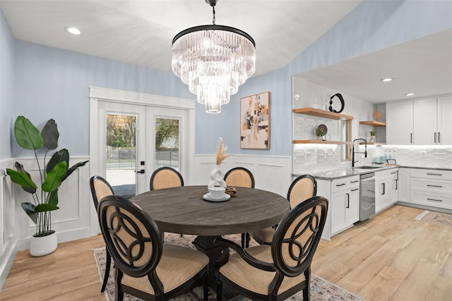 dining space featuring light wood finished floors, a notable chandelier, french doors, wainscoting, and a decorative wall