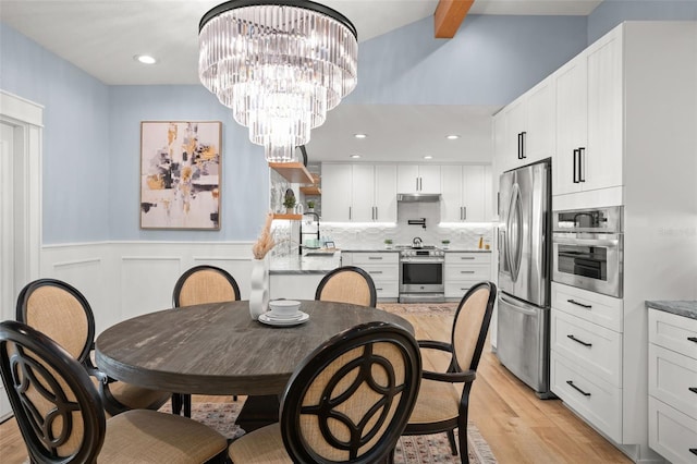 dining area featuring beam ceiling, recessed lighting, wainscoting, an inviting chandelier, and light wood-style floors