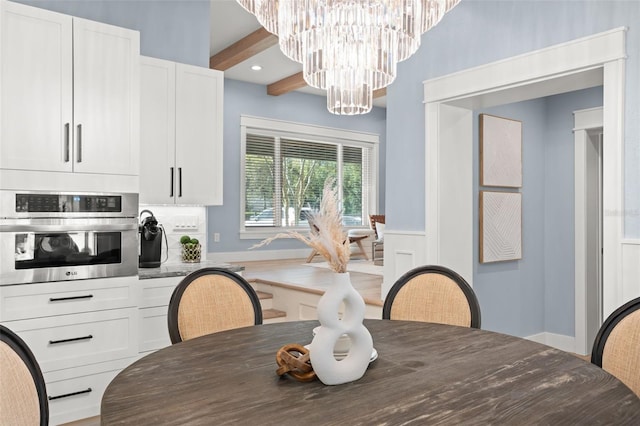 dining area featuring beamed ceiling, an inviting chandelier, and wainscoting