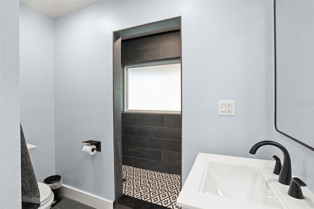 bathroom featuring a sink, baseboards, toilet, and a tile shower