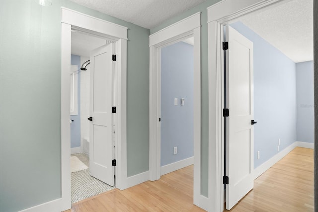 hall featuring baseboards, a textured ceiling, and light wood-style floors