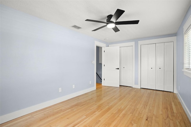 unfurnished bedroom featuring visible vents, two closets, hardwood / wood-style floors, baseboards, and ceiling fan