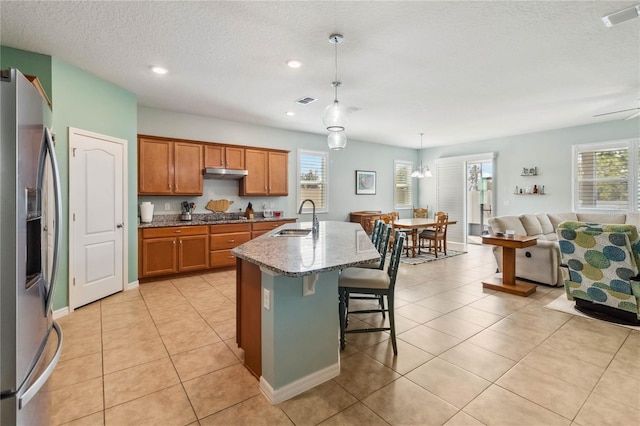 kitchen with visible vents, under cabinet range hood, appliances with stainless steel finishes, brown cabinetry, and a sink