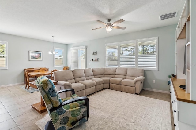 living area featuring light tile patterned flooring, ceiling fan with notable chandelier, visible vents, and baseboards