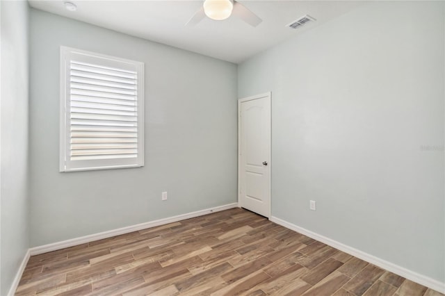 spare room with a ceiling fan, wood finished floors, visible vents, and baseboards