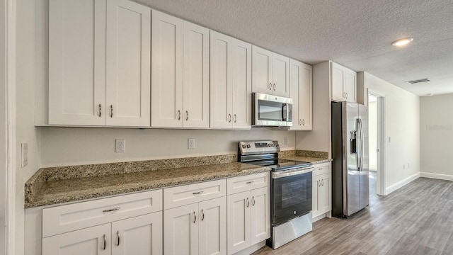 5963 Virtudes St, Sebring, FL 33872 - kitchen featuring appliances with stainless steel finishes, white cabinetry, a textured ceiling, light wood-style floors, and light stone counters