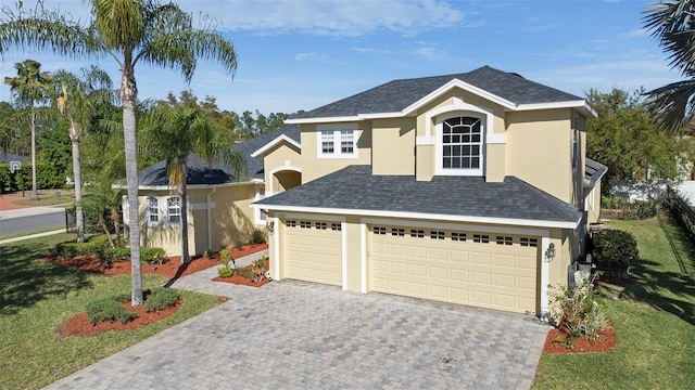 traditional-style home featuring stucco siding, an attached garage, a shingled roof, and decorative driveway