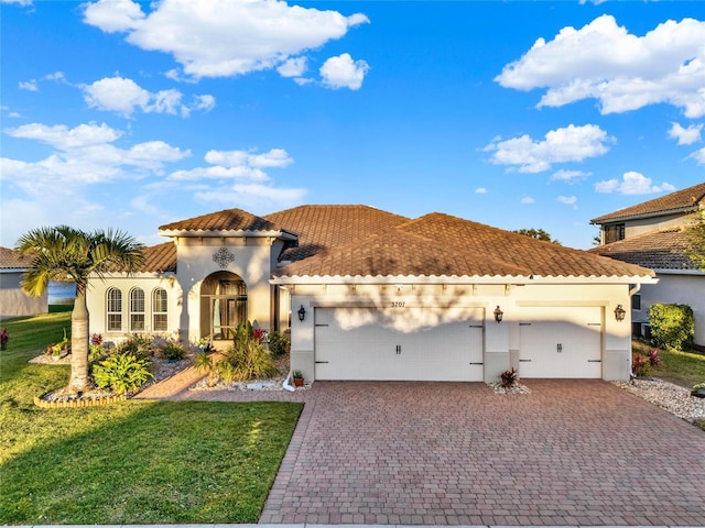 mediterranean / spanish house featuring a front lawn, a tile roof, stucco siding, decorative driveway, and a garage