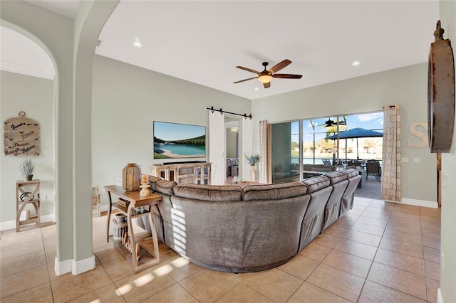 living area featuring light tile patterned floors, baseboards, a barn door, and a ceiling fan