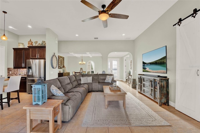 living area with a barn door, recessed lighting, ceiling fan with notable chandelier, light tile patterned flooring, and arched walkways