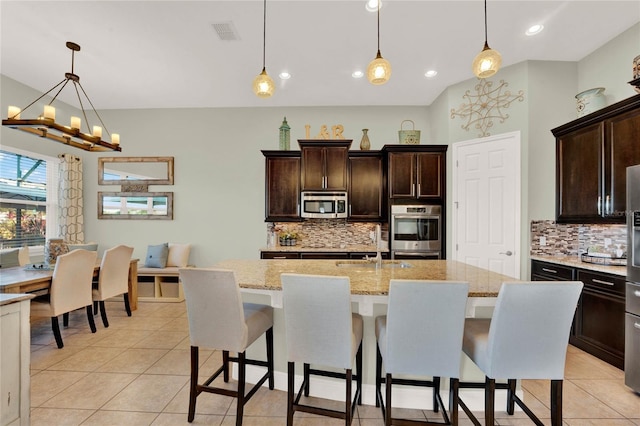 kitchen featuring visible vents, pendant lighting, a kitchen island with sink, dark brown cabinetry, and appliances with stainless steel finishes