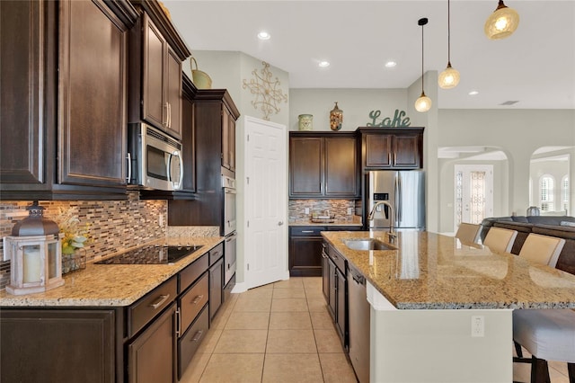 kitchen with dark brown cabinetry, a breakfast bar, appliances with stainless steel finishes, arched walkways, and a sink