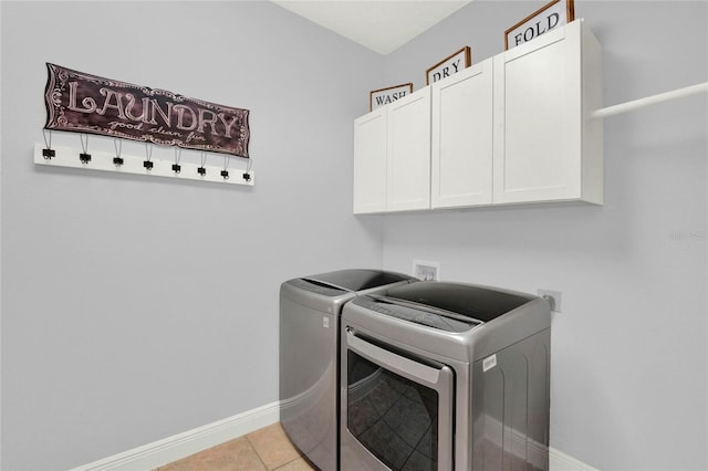 clothes washing area featuring washer and dryer, light tile patterned flooring, cabinet space, and baseboards