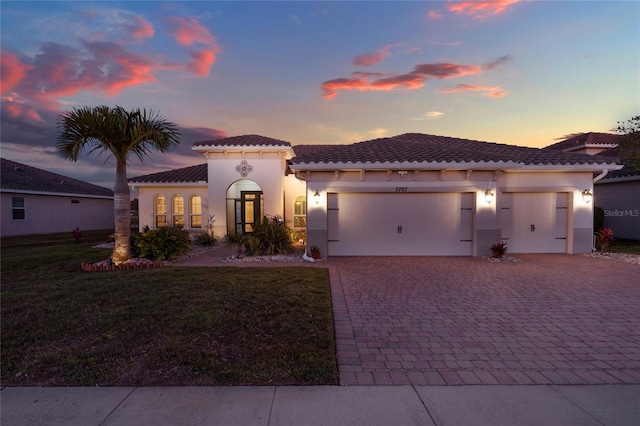 mediterranean / spanish house with a front lawn, a tile roof, stucco siding, decorative driveway, and an attached garage