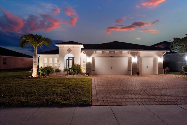 mediterranean / spanish-style home featuring decorative driveway, a lawn, an attached garage, and stucco siding