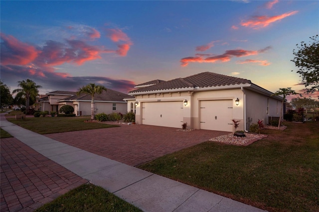 mediterranean / spanish home with an attached garage, stucco siding, a front lawn, a tiled roof, and decorative driveway