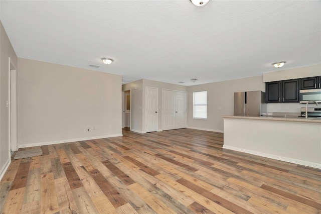 unfurnished living room with light wood-style floors, visible vents, and baseboards