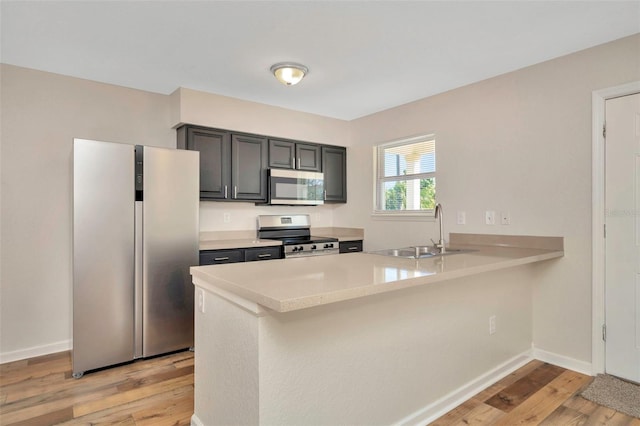 kitchen featuring a sink, light wood-style floors, appliances with stainless steel finishes, a peninsula, and light countertops