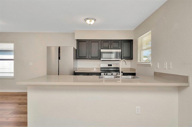 kitchen featuring baseboards, light countertops, light wood-style flooring, stainless steel appliances, and a sink