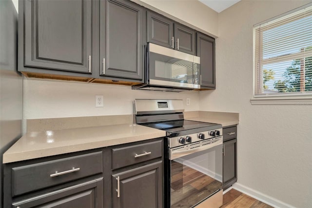 kitchen featuring light countertops, baseboards, light wood-type flooring, and stainless steel appliances