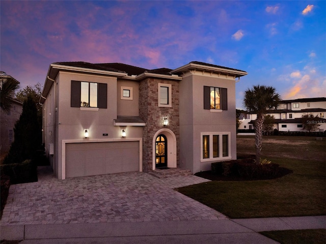 mediterranean / spanish home featuring stone siding, stucco siding, an attached garage, and decorative driveway