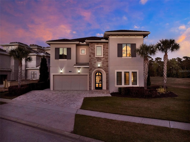 mediterranean / spanish home featuring a front yard, stucco siding, decorative driveway, a garage, and stone siding