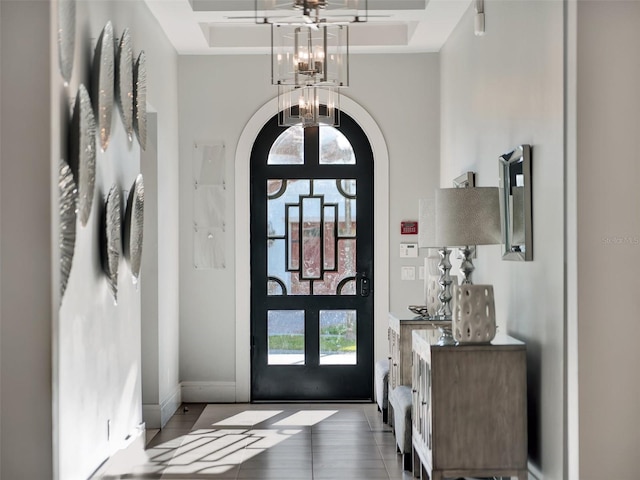 entryway featuring baseboards, a tray ceiling, an inviting chandelier, a towering ceiling, and arched walkways