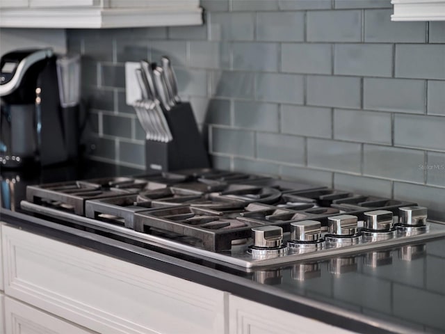 interior details with tasteful backsplash, dark countertops, white cabinets, and stainless steel gas cooktop