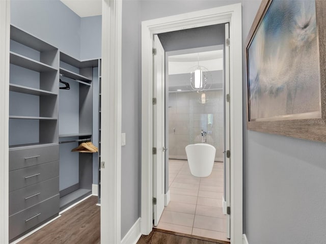 full bath featuring a spacious closet, a freestanding tub, baseboards, and wood finished floors