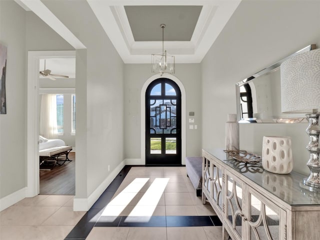 foyer entrance featuring an inviting chandelier, a raised ceiling, light tile patterned floors, and baseboards