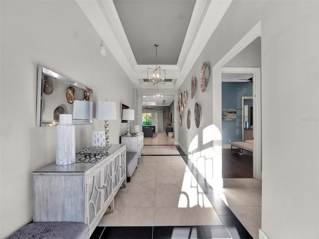 foyer entrance with a raised ceiling, ornamental molding, baseboards, and a chandelier