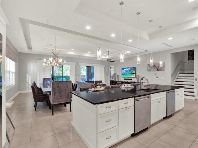 kitchen featuring a tray ceiling, an island with sink, a sink, dark countertops, and open floor plan