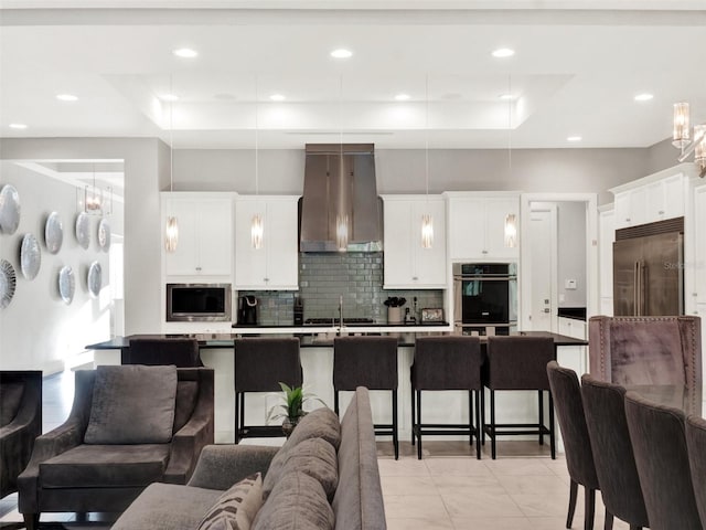 kitchen with a tray ceiling, ventilation hood, open floor plan, and built in appliances