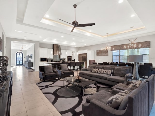 living room featuring light tile patterned floors, baseboards, a tray ceiling, recessed lighting, and ceiling fan with notable chandelier