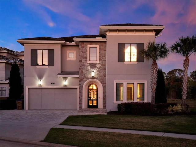 view of front of home with stucco siding, a lawn, decorative driveway, stone siding, and an attached garage