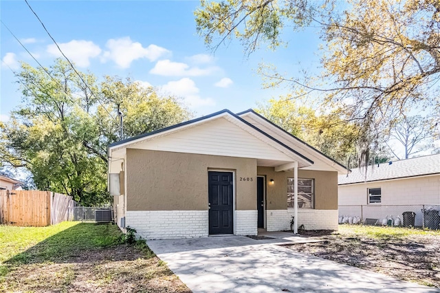 bungalow-style home featuring brick siding, stucco siding, central AC, and fence