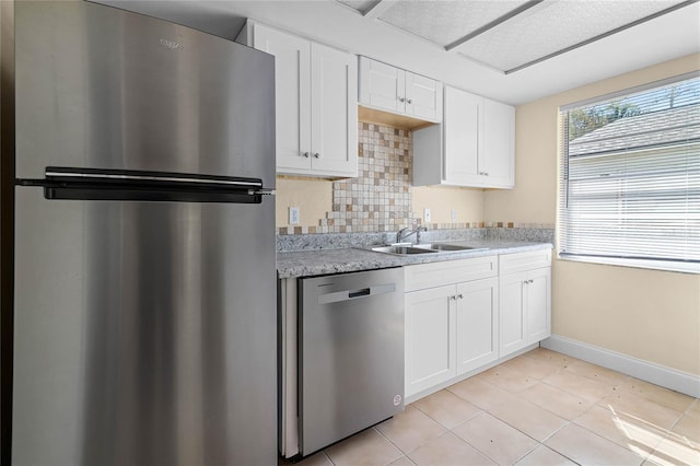 kitchen featuring baseboards, a sink, stainless steel appliances, white cabinetry, and tasteful backsplash