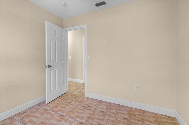 spare room featuring light tile patterned flooring, baseboards, visible vents, and a textured ceiling