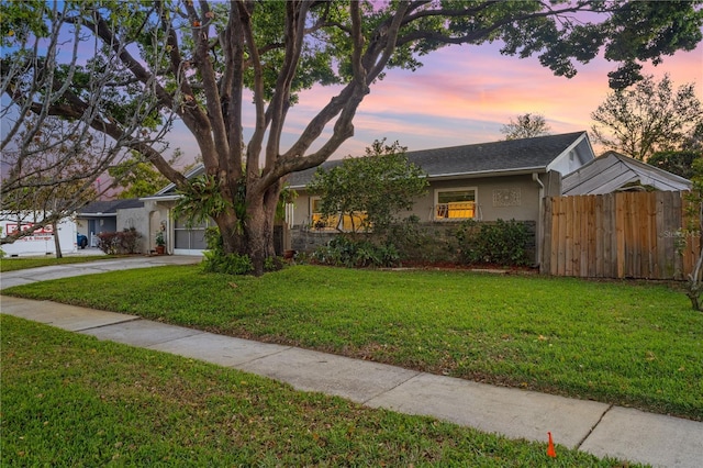 view of front of home featuring fence, driveway, stucco siding, stone siding, and a lawn