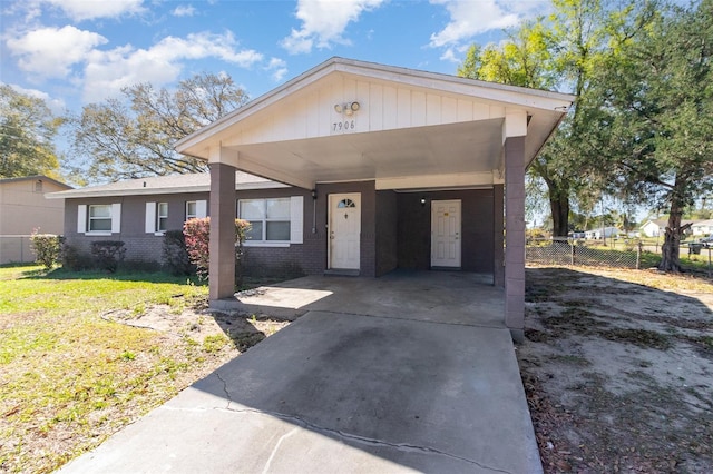 view of front facade featuring brick siding, an attached carport, fence, concrete driveway, and a front yard