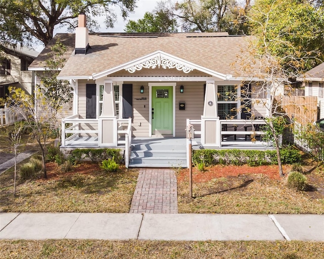 view of front of property featuring roof with shingles, covered porch, and a chimney