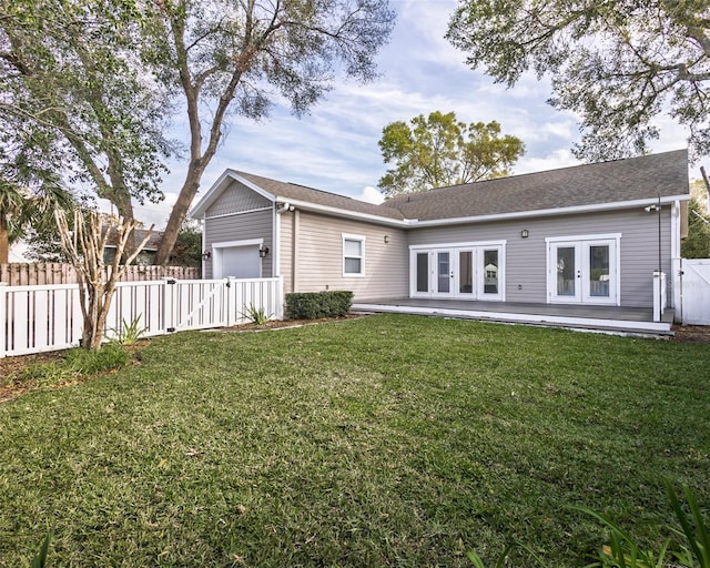 rear view of property featuring french doors, a yard, an attached garage, and fence