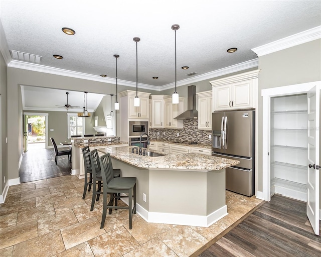 kitchen featuring light stone counters, decorative backsplash, stainless steel appliances, wall chimney exhaust hood, and a sink