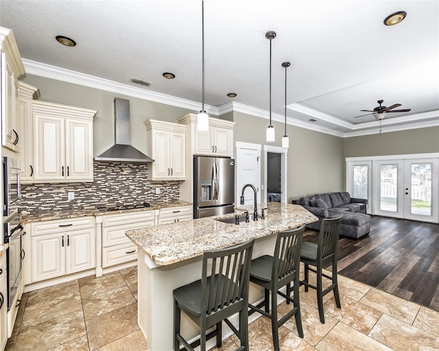 kitchen with a sink, light stone counters, french doors, appliances with stainless steel finishes, and wall chimney exhaust hood