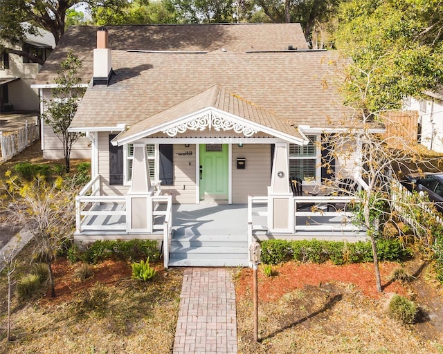 view of front facade featuring fence, covered porch, a chimney, and a shingled roof