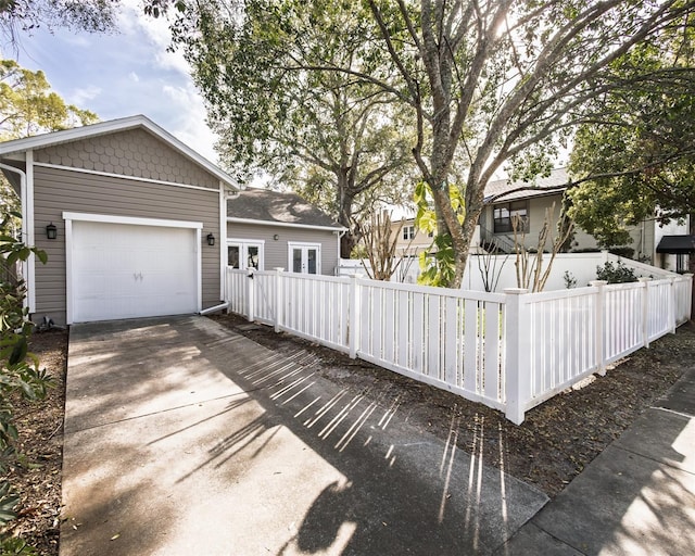 view of front of property with a fenced front yard, an attached garage, concrete driveway, and french doors