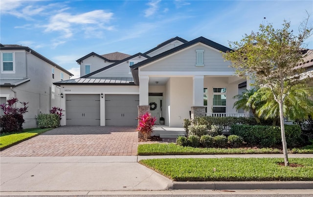 craftsman house featuring stucco siding, metal roof, decorative driveway, an attached garage, and a standing seam roof