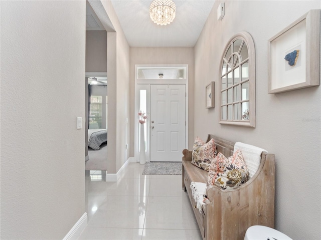 foyer entrance with an inviting chandelier, light tile patterned floors, a textured wall, and baseboards