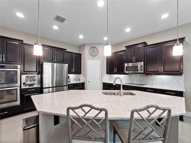 kitchen with backsplash, a breakfast bar area, light tile patterned floors, appliances with stainless steel finishes, and a sink